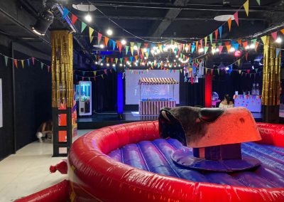 Montaje de feria americana con toro mecánico y puestos de juego para eventos de empresa en espacios interiores