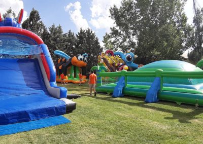 Vista de un campo de césped con varios hinchables grandes (azul, verde) instalados para una fiesta escolar de fin de curso en un colegio.