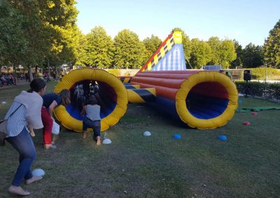 Circuito de obstáculos hinchable con túneles y rampas de gran formato instalado en una zona de césped para un evento escolar multitudinario.